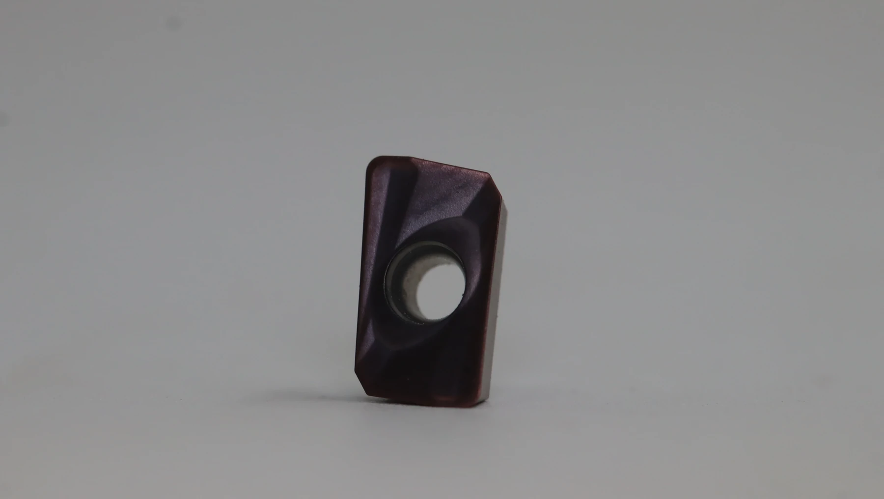 Two black carbide inserts, the front one square to camera showing the concentric machining rings inside its gold bore