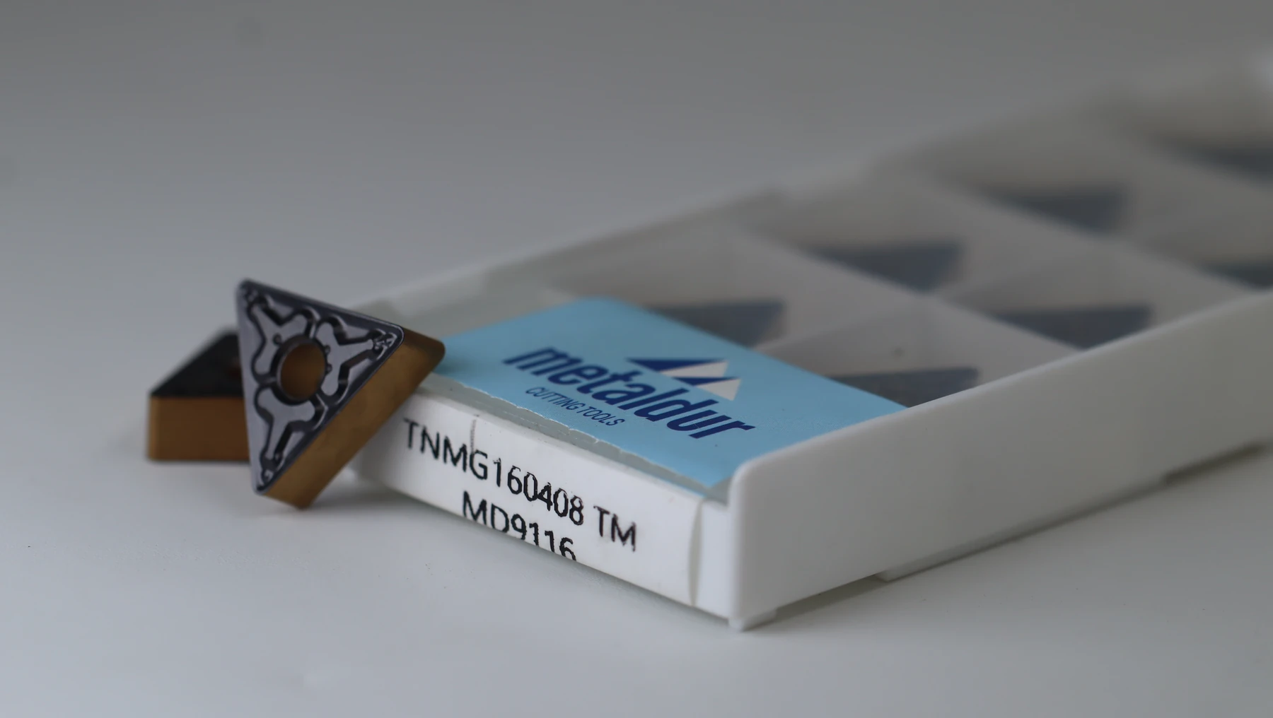 A boxed set of copper-toned inserts shot at a shallow angle, the grade label CCMT09T304 reading along the lower edge