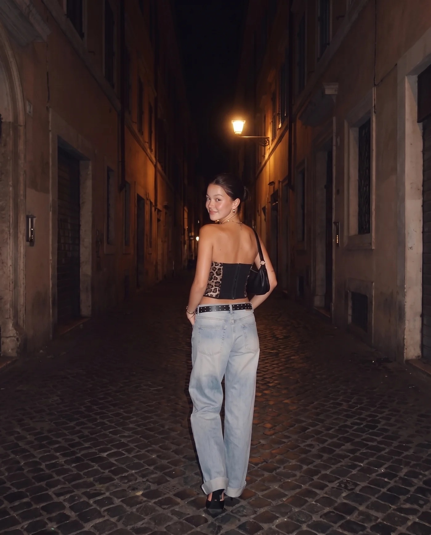 Casuall leopard-print corset — walking a cobbled street at night, shot from behind under streetlight