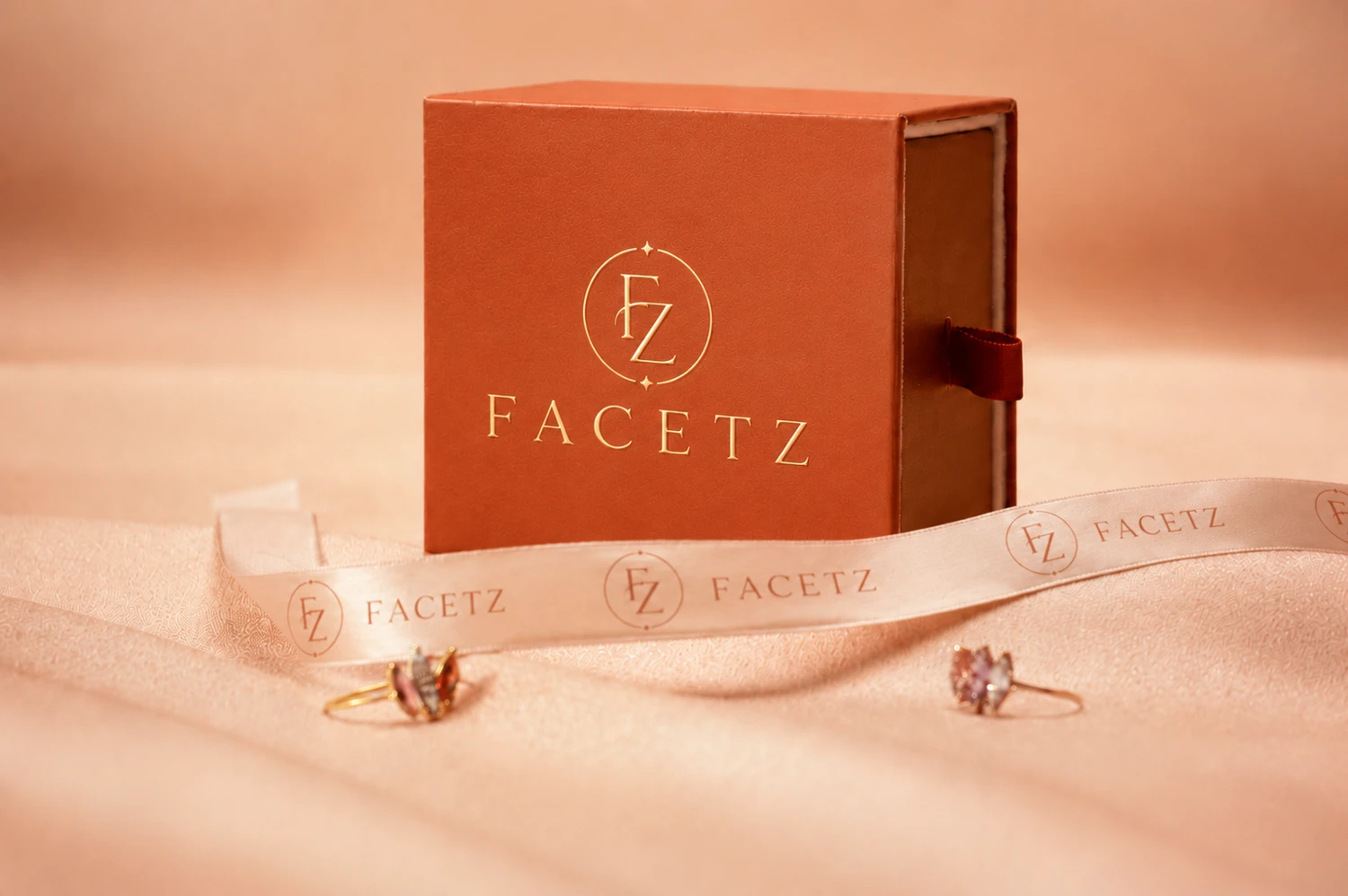FACETZ packaging — a terracotta rigid box with foil monogram and printed ribbon