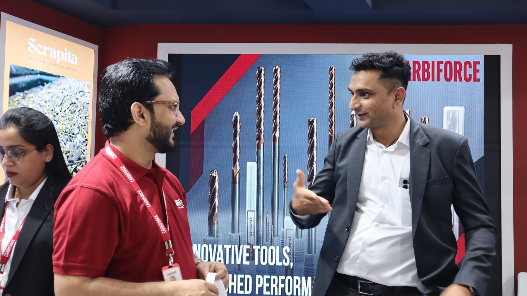 Two men in conversation in front of a large backlit drill graphic on the stand wall