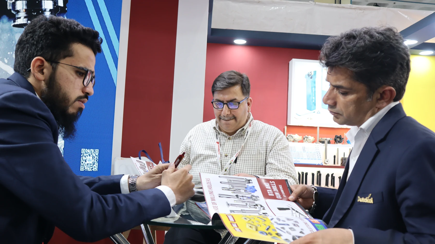 Three men around a meeting table with a product catalogue open between them
