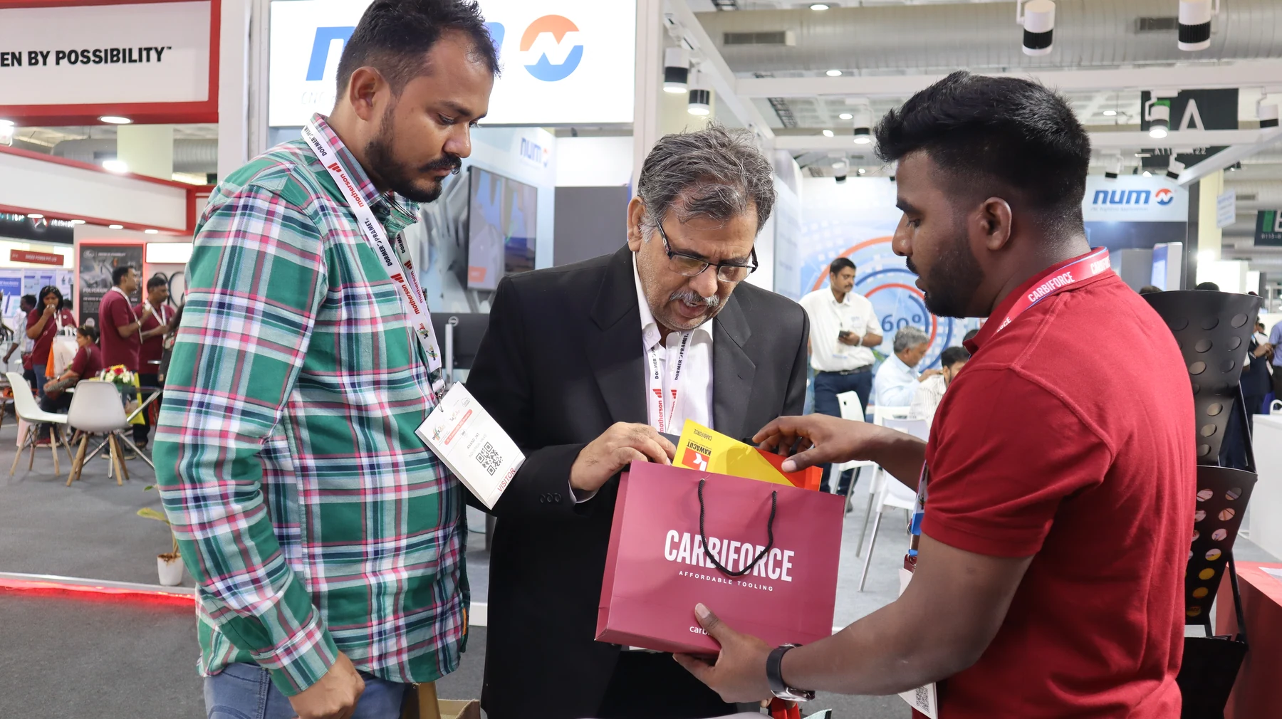 A second handover, a visitor in a checked shirt taking a catalogue bag from a team member