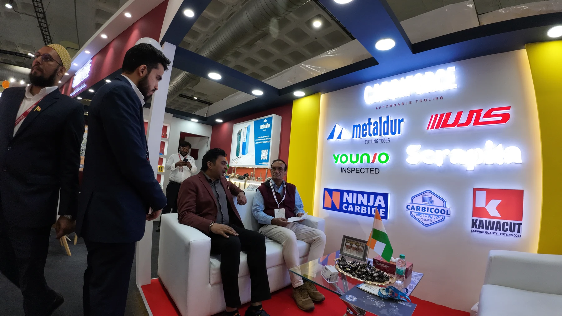 Visitors seated on the stand's white sofas in front of the wall of partner brand marks