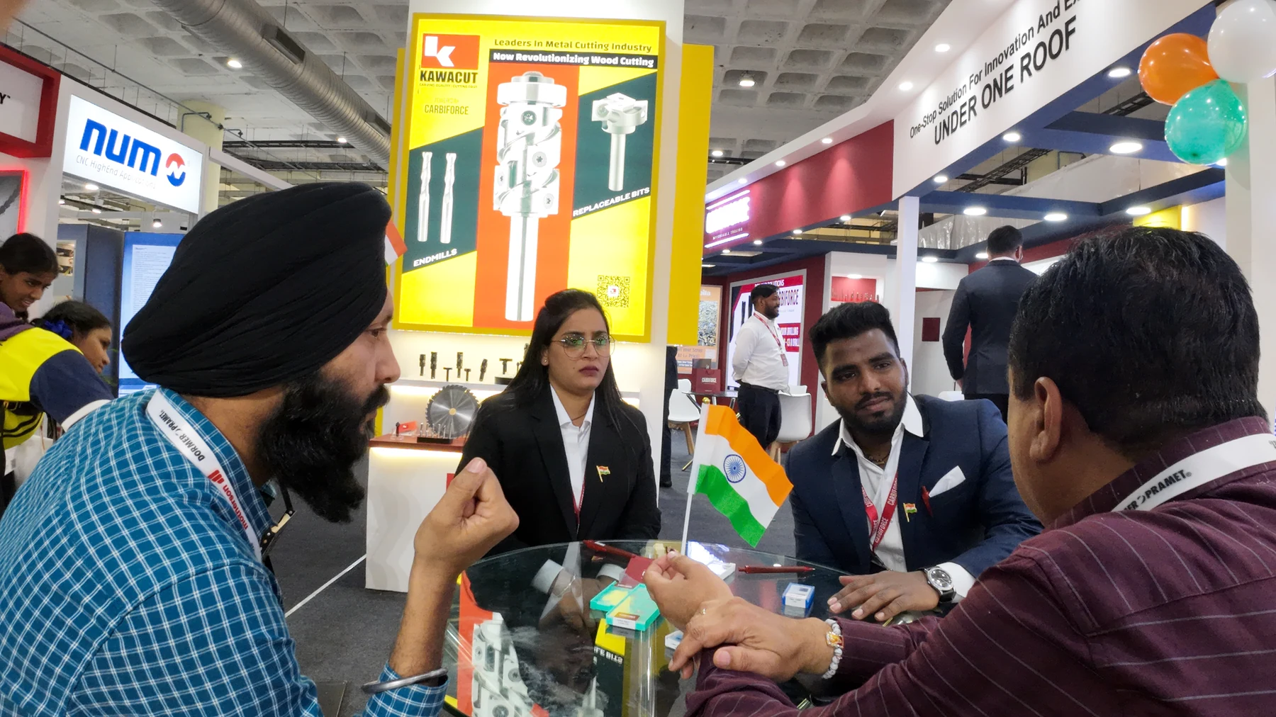 A group of visitors and staff around a glass table mid-conversation, the busy stand behind